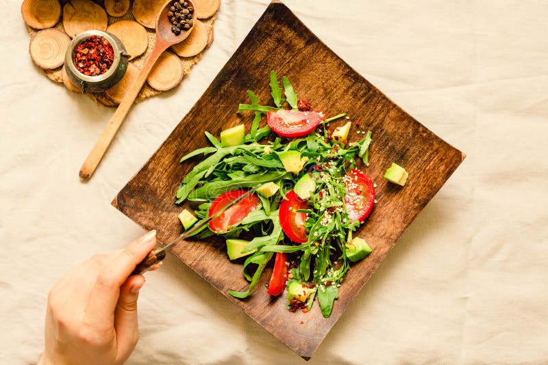 Fresh light green salad with avocado and tomatoes in a wooden plate. Top view. The process of eating. royalty free stock image Fresh light green salad with avocado and tomatoes in a wooden plate. Top view. The process of eating. royalty free stock image