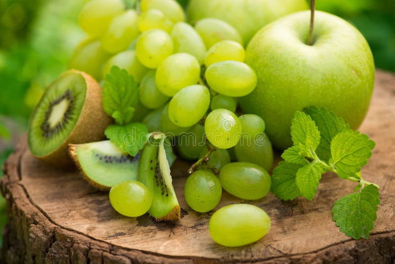 Fresh natural green fruits apple, grapes, kiwi and mint leaf on a wooden stump in garden