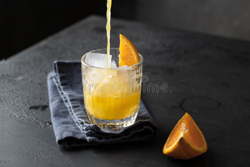 Fresco naranja jugo fundición vaso sobre el oscuro.