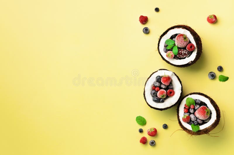 Fresh organic berries, mint leaves inside ripe coconuts on yellow background with copy space. Top View. Pop art design stock image Fresh organic berries, mint leaves inside ripe coconuts on yellow background with copy space. Top View. Pop art design stock image