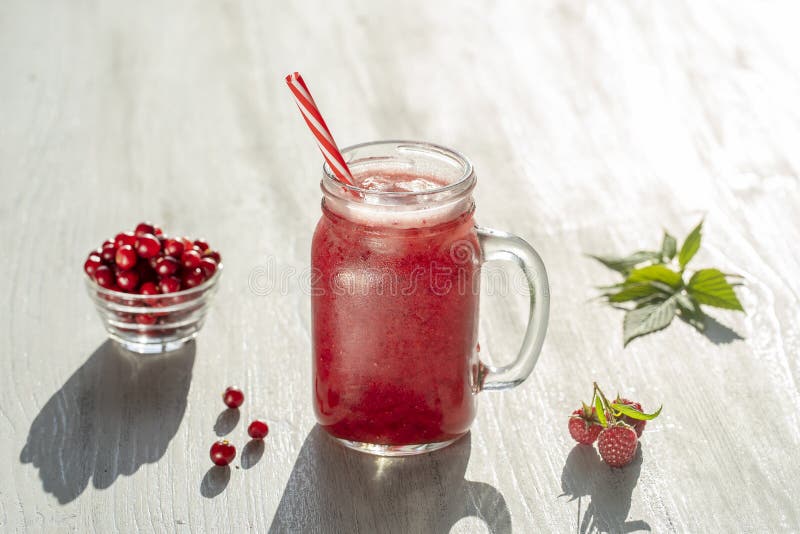 Fresh organic red smoothie in glass mug on white table, close up. Refreshing summer fruit drink. The concept of healthy eating.