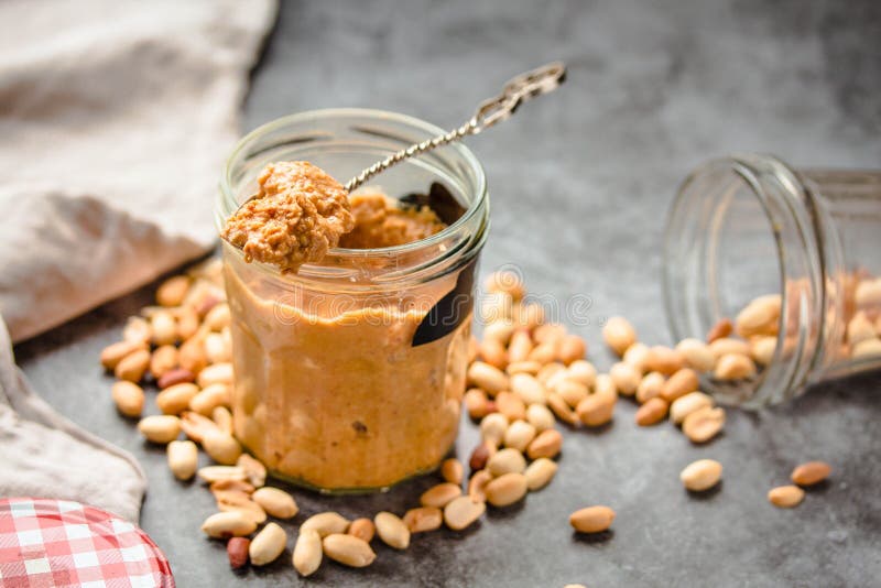 Fresh Peanut Spread in Jar and Spoon and Scattered Peanuts on Gray