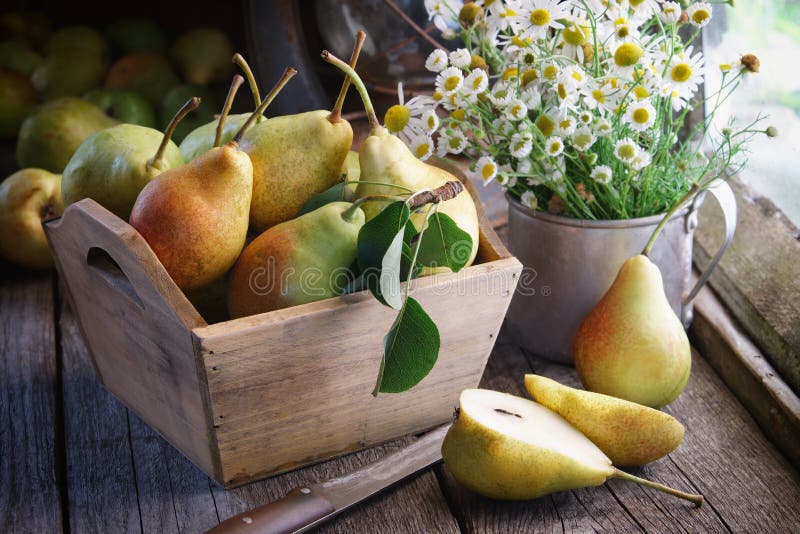 Fresh pears in a wooden crate and bouquet of daisies on wooden table.