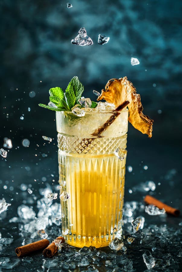 Fresh pineapple cocktail with cinnamon and ice in jar glass on dark blue background.