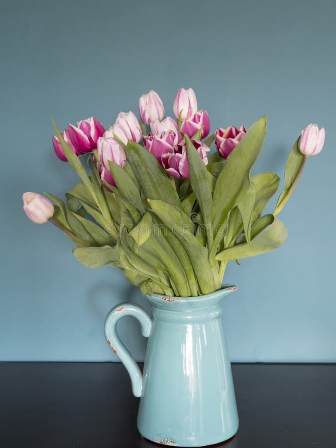 Fresh pink and red tulip flowers bouquet on shelf in front of green wall. View with copy space