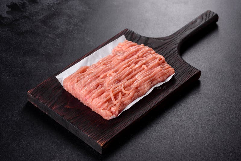 Fresh raw chicken mince on a dark wooden cutting board