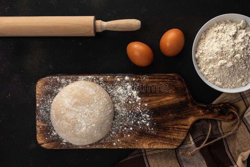 Fresh raw dough for bread or pizza with eggs on a dark background with dusting of flour. Top view. Raw fresh yeast dough stock images, royalty-free photos and pictures