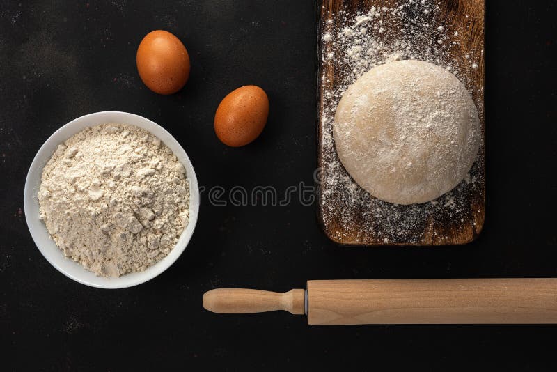 Fresh raw dough for bread or pizza with eggs on a dark background with dusting of flour. Top view. Raw fresh yeast dough stock images, royalty-free photos and pictures