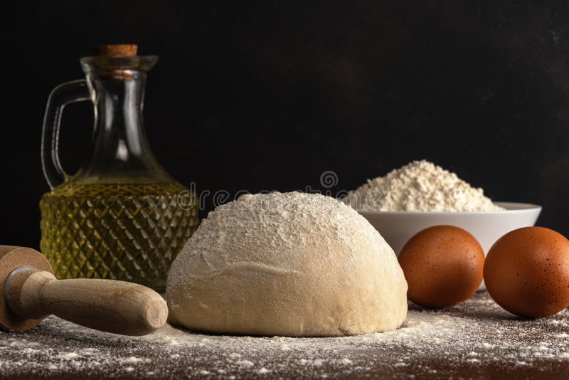 Fresh raw dough for bread or pizza with eggs and oil on a dark wooden table. Raw fresh yeast dough stock images, royalty-free photos and pictures