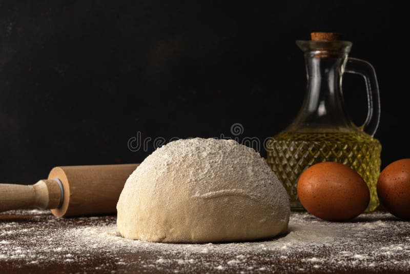 Fresh raw dough for bread or pizza with eggs and oil on a dark wooden table. Raw fresh yeast dough stock images, royalty-free photos and pictures