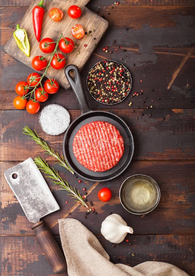 Fresh raw minced homemade farmers grill beef burger in frying pan with spices and herbs and meat hatchet on wooden board. Oil, royalty free stock photos Fresh raw minced homemade farmers grill beef burger in frying pan with spices and herbs and meat hatchet on wooden board. Oil, royalty free stock photos