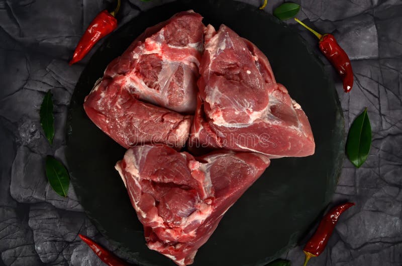 Fresh raw mutton shoulder meat isolated on black stone background with spices