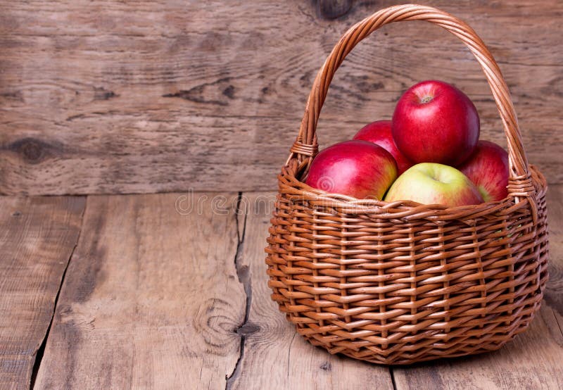 Fresh red apples in basket over wooden background