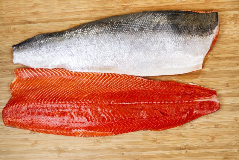 Horizontal photo of two Red Salmon fillets, one skin side up, on natural bamboo cutting board. Horizontal photo of two Red Salmon fillets, one skin side up, on natural bamboo cutting board