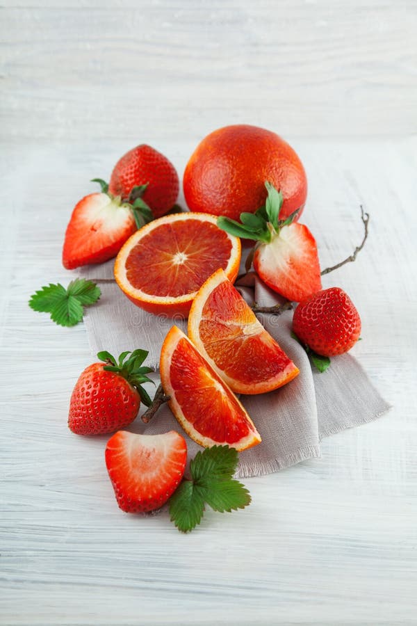 Fresh ripe blood oranges and strawberries, slices, rustic food photography on white wood plate