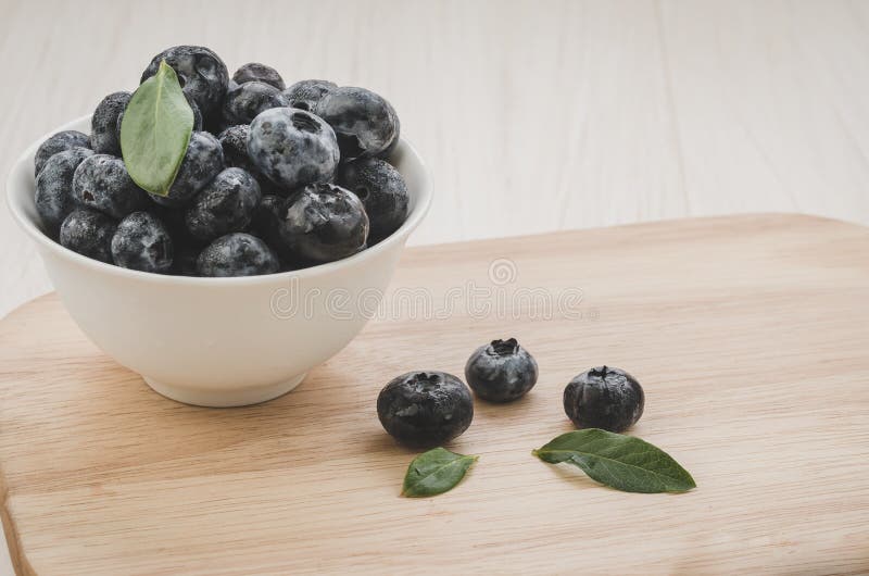 Fresh ripe blueberries with leaves in bowl on wooden tray/Fresh ripe blueberries with leaves in bowl on wooden tray. Copy space. stock photo Fresh ripe blueberries with leaves in bowl on wooden tray/Fresh ripe blueberries with leaves in bowl on wooden tray. Copy space. stock photo