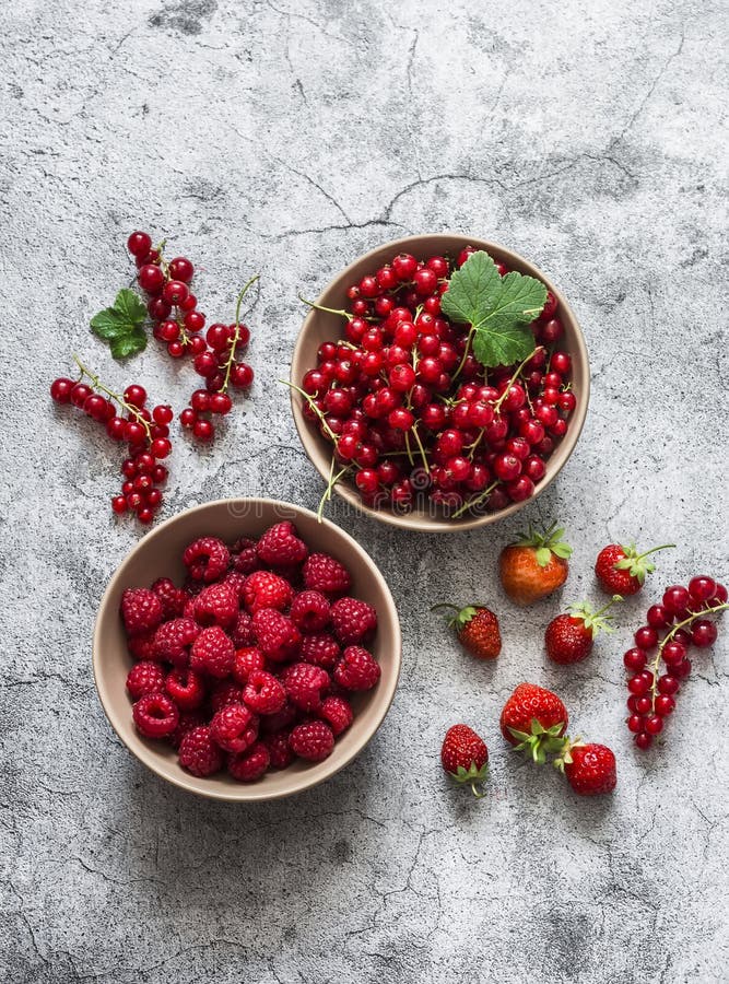 Fresh ripe garden organic berries in bowls - raspberries, red currant strawberries on a gray background, top view