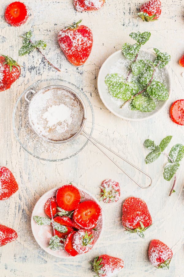 Fresh ripe strawberries with mint leaves and icing sugar on white wooden background