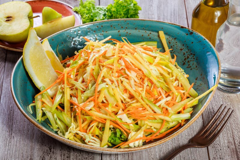 Fresh salad with apple, carrot, cabbage, celery and lemon on wooden background close up. Healthy food.