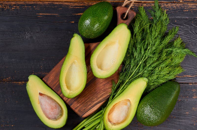 Fresh sliced avocados and dill on the wooden board. Raw ingredients for veggie healthy or diet dish on the black background