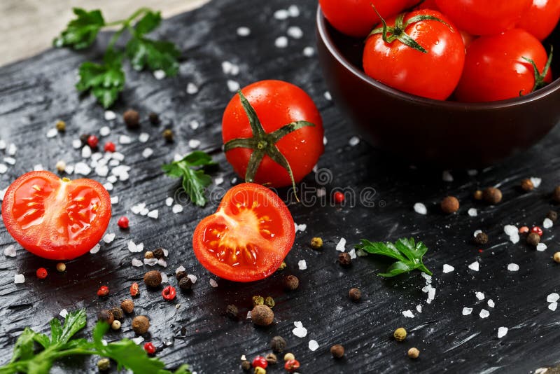 Fresh Sliced Cherry Tomatoes on a black background with spices coarse salt and herbs. Top view, use as cooking ingredients