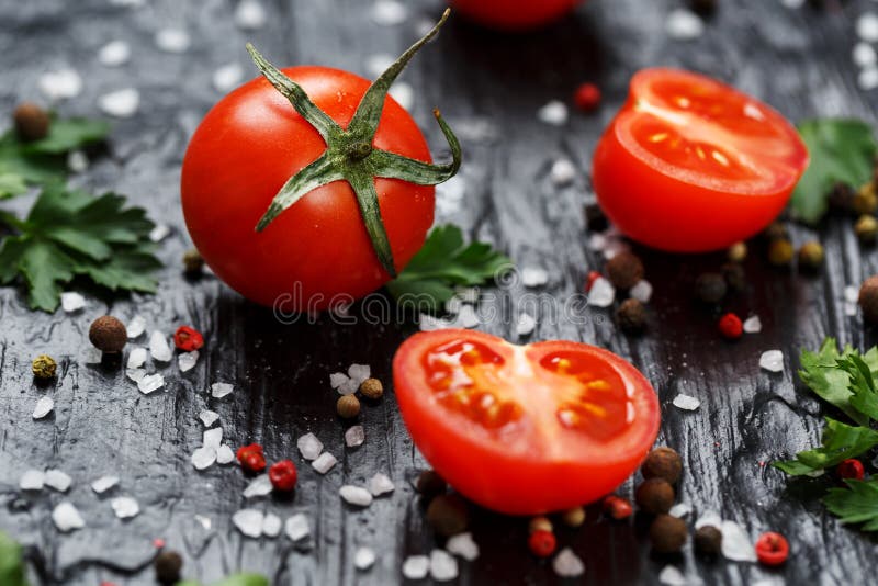 Fresh Sliced Cherry Tomatoes on a black background with spices coarse salt and herbs. Top view, use as cooking ingredients