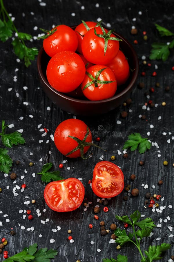 Fresh Sliced Cherry Tomatoes on a black background with spices coarse salt and herbs. Top view, use as cooking ingredients