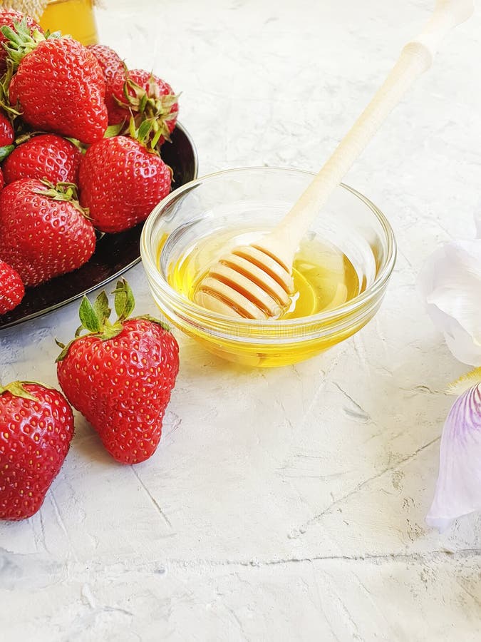 Fresh strawberries on a plate, honey, iris flower on a gray concrete background