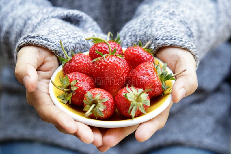 Fresh strawberries on a yellow plate in woman`s hands. Selectiv