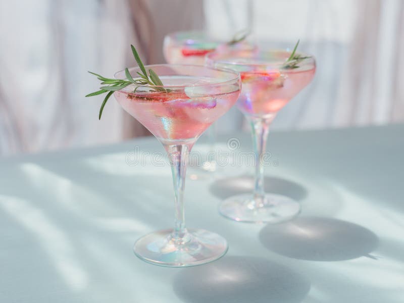 Fresh strawberry cocktail. Summer pink cocktail with strawberry, rosemary and ice cubes on light blue background mockup. Trendy