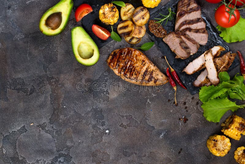 Fresh three types of grilled steak chicken, pork, beef on slate plate with herbs, tomato, avocado and grilled potatoes