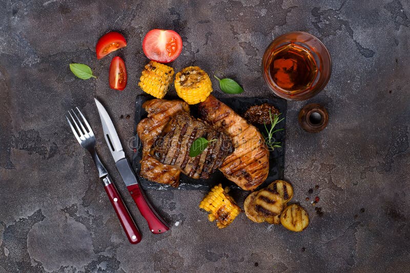 Fresh three types of grilled steak chicken, pork, beef on slate plate with herbs, tomato, juice and grilled potatoes