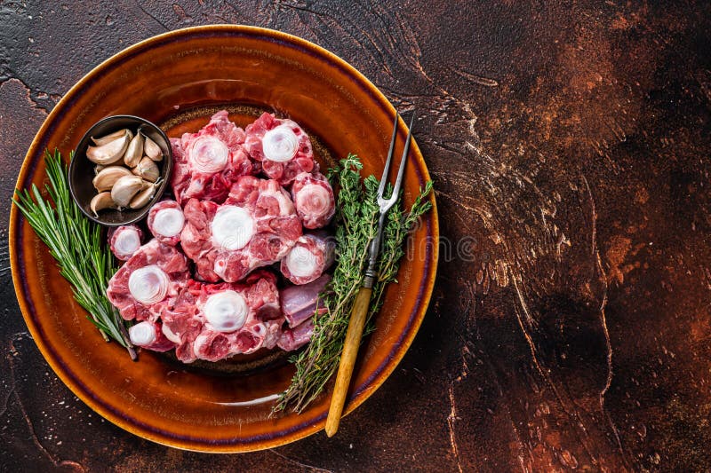 Fresh Uncooked Beef Oxtail Cut Meat on Rustic Plate with Herbs. Dark