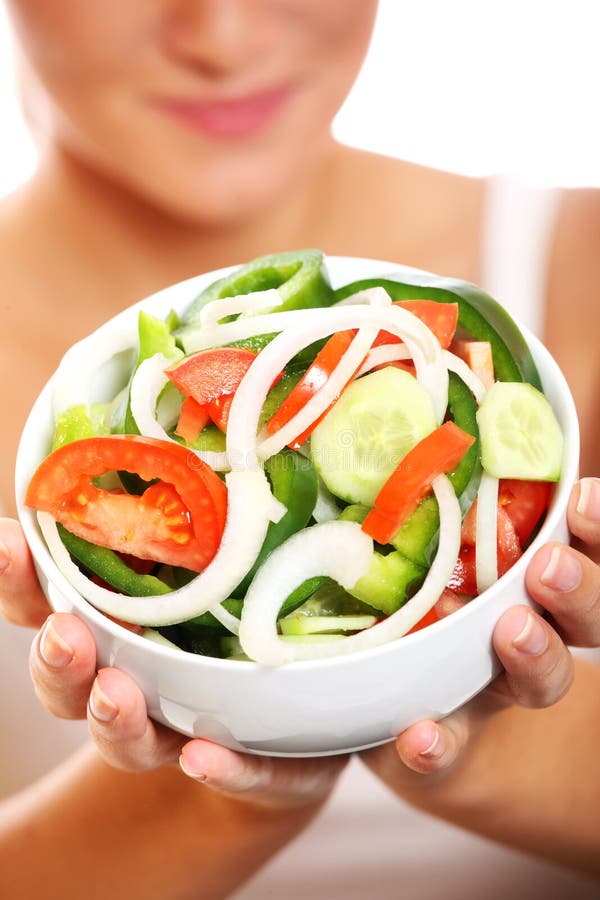 A close-up of a fresh vegetable salad with a pretty woman holding it in the background