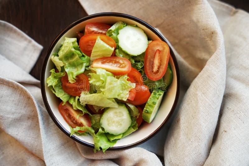 fresh vegetable salad of green cucumbers, cherry tomatoes and iceberg lettuce, with olive oil in a deep plate