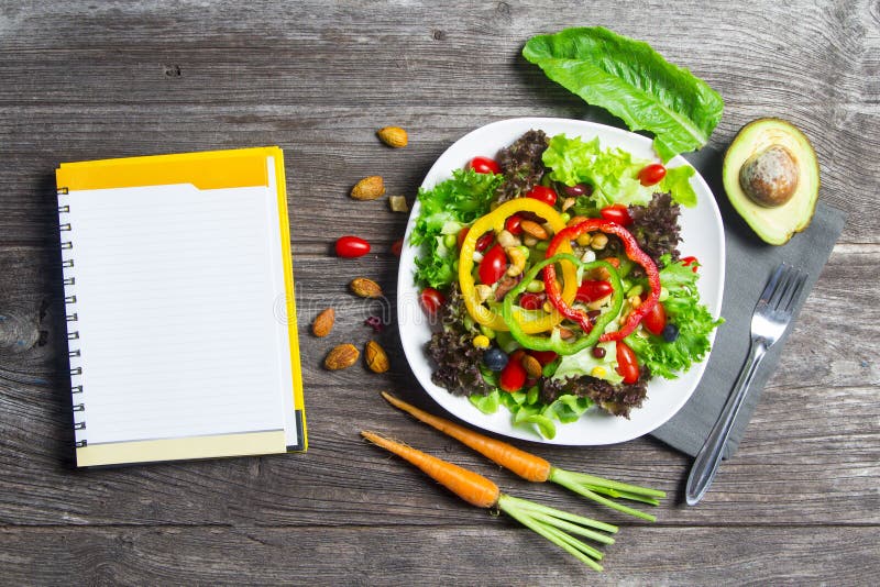 Fresh vegetable salad with notebook paper on wood table background, top view