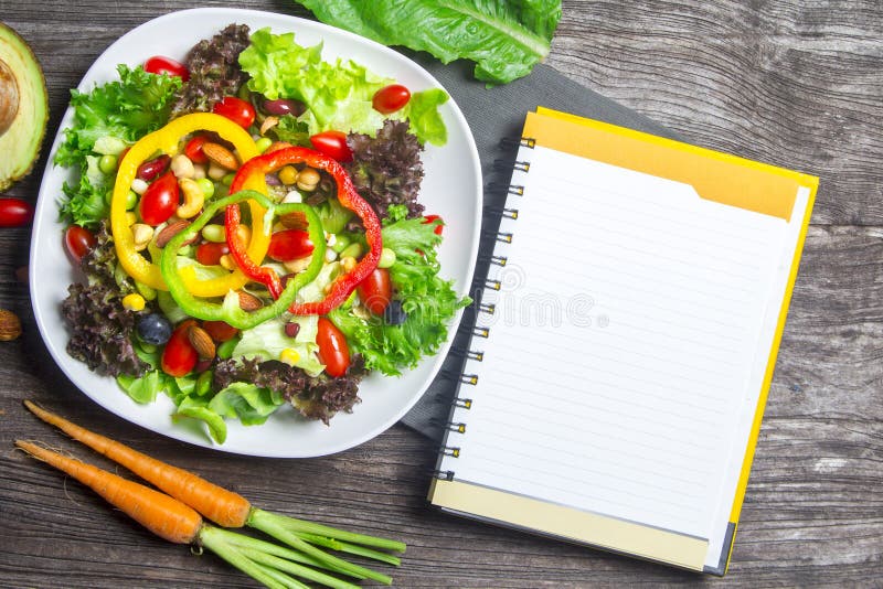 Fresh vegetable salad with notebook paper on wood table background, top view