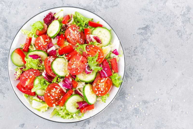 Fresh vegetable salad with tomatoes, cucumbers, sweet pepper and sesame seeds. Vegetable salad on white plate