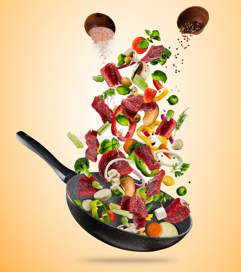 Fresh vegetables and beef meat flying into a pan on brown background