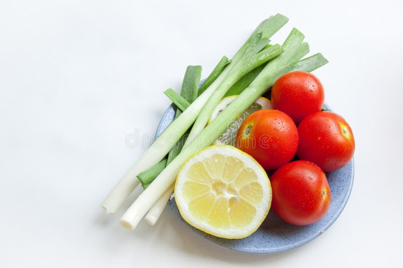 Fresh vegetables (onions, tomato and lemon) on a blue plate stock photo