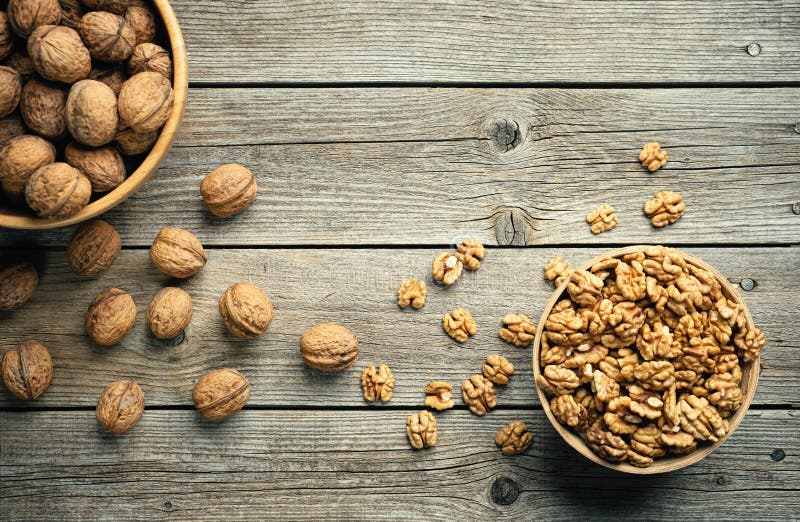 Fresh walnut kernels and whole walnuts in a bowl on rustic old wooden table.