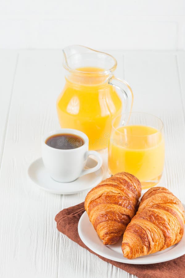 Freshly baked croissant, orange juice, fresh fruits, jam on white wooden background. French breakfast. Fresh pastries for morning.