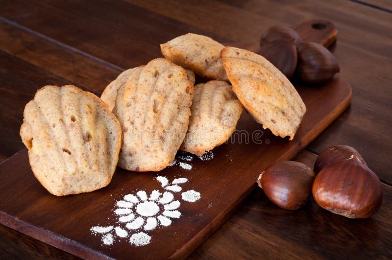 Freshly baked madelines. Festive madeleines baked with chestnut and served on a wooden board for a Christmas treat. A traditional French tea cake formed in a stock photo Freshly baked madelines. Festive madeleines baked with chestnut and served on a wooden board for a Christmas treat. A traditional French tea cake formed in a stock photo
