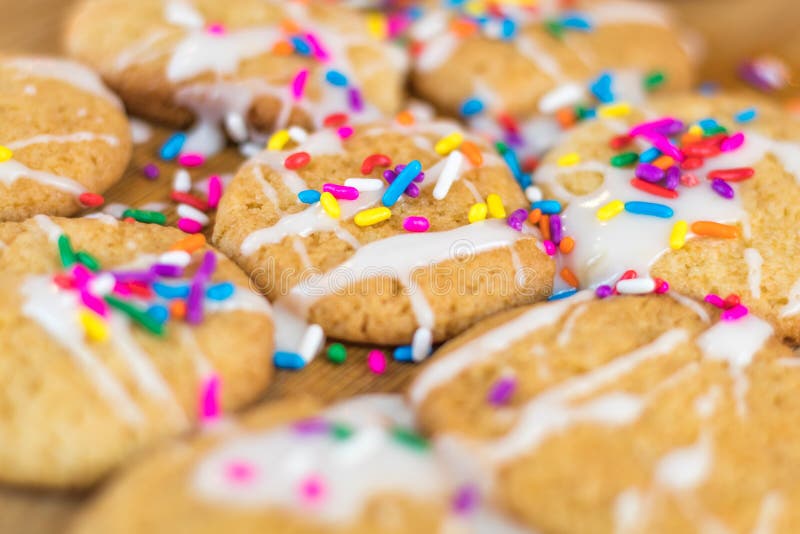 Freshly baked sugar cookies with white icing and rainbow colored sprinkles on wooden board, selective focus