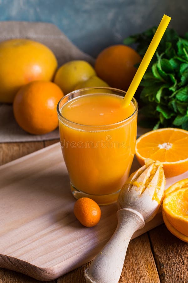 Freshly pressed citrus fruit juice from oranges lemons limes cumquat, glass with straw, reamer, mint on table by window, rustic stock image