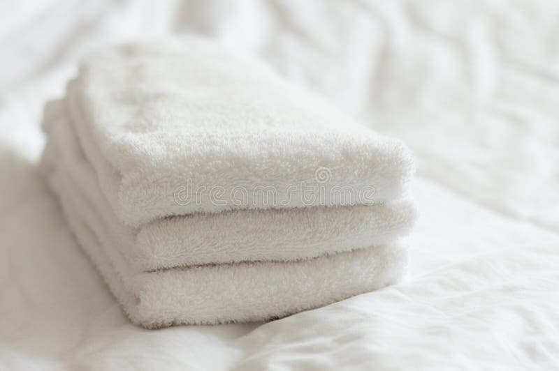 Freshly washed white hand towels stacked on a white bed in a bedroom with diffused light. Freshly washed white hand towels stacked on a white bed in a bedroom with diffused light.