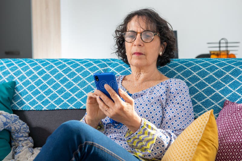 Freuen Sie sich auf eine junge Frau, die mit ihrem Smartphone auf dem Sofa sitzt stockfotos