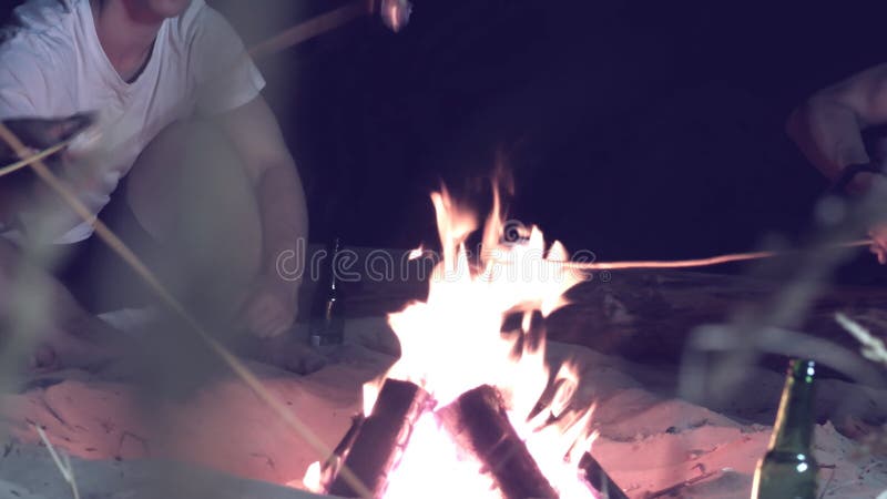 Freunde, die Eibische um ein Lagerfeuer am Abend auf dem Strand braten