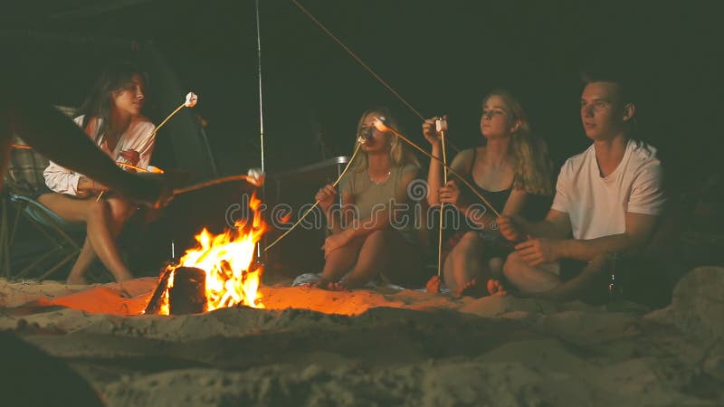 Freunde, die Eibische um ein Lagerfeuer am Abend auf dem Strand braten