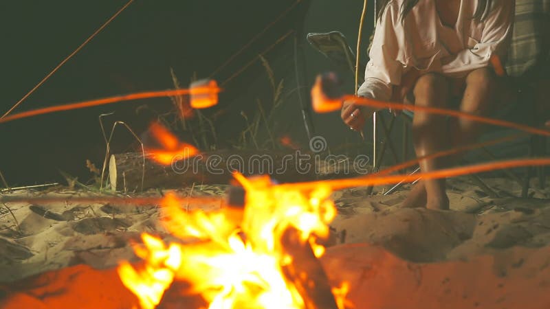 Freunde, die Eibische um ein Lagerfeuer am Abend auf dem Strand braten